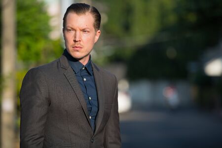 Portrait of young handsome businessman in suit looking back outdoors