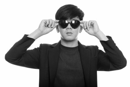 Studio shot of cool handsome Asian businessman wearing and holding heart shaped sunglassesの写真素材