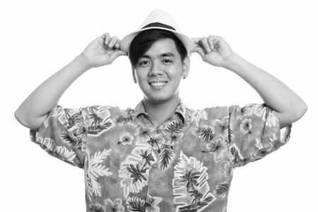 Young happy Asian tourist man smiling while holding hat with both hands