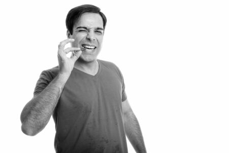 Studio shot of young happy Persian man smiling while biting red chili pepper isolated against white backgroundの写真素材