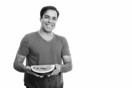 Studio shot of young happy Persian man smiling while holding slice of watermelon isolated against white backgroundの写真素材