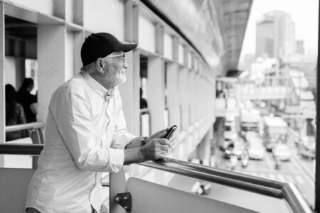 Handsome bearded senior tourist man exploring the city in black and white