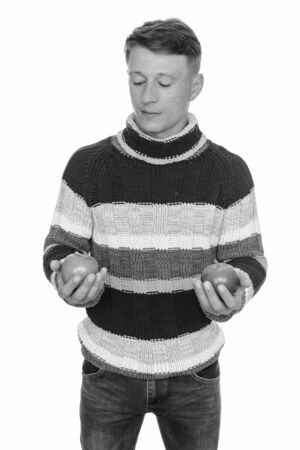 Studio shot of young handsome Caucasian man holding green and red apple isolated against white backgroundの写真素材
