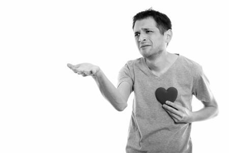 Studio shot of sad young man giving hand with red heart on chest ready for Valentines dayの写真素材