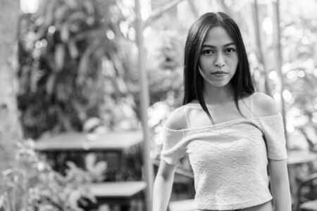 Young beautiful Asian teenage girl at relaxing green garden surrounded with healthy plants and treeの写真素材