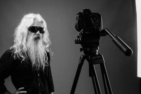 Senior man with long hair and beard vlogging in black and whiteの写真素材