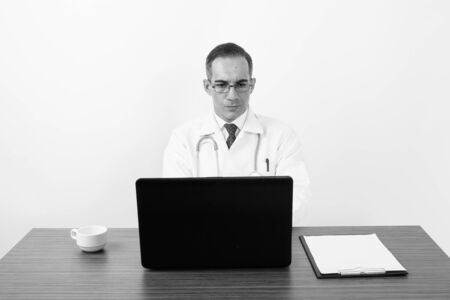 Mature Persian man doctor behind desk in black and whiteの写真素材