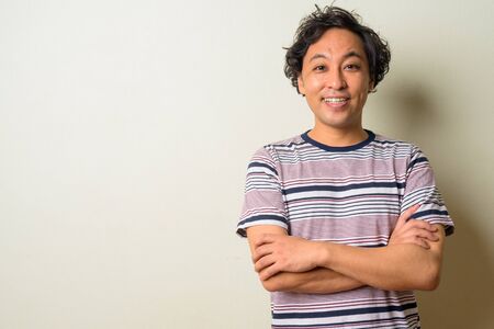 Portrait of happy Japanese man with curly hair smiling with arms crossedの写真素材