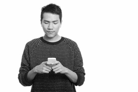Studio shot of young Asian man using mobile phoneの写真素材
