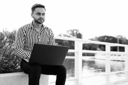 Young bearded Indian businessman relaxing at the park in the cityの写真素材