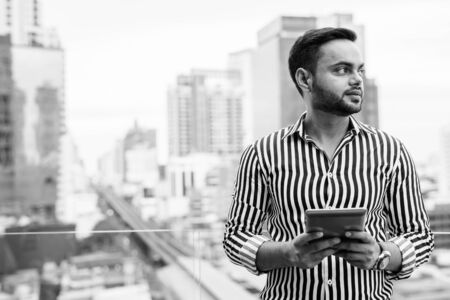 Young bearded Indian businessman against view of the cityの写真素材