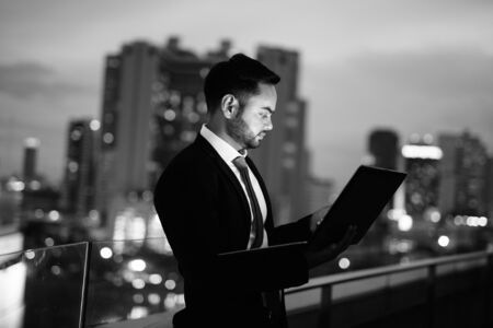 Young bearded Indian businessman against view of the city at nightの写真素材