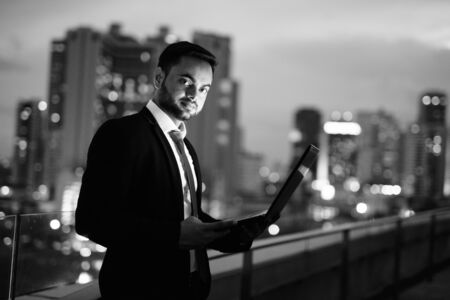 Young bearded Indian businessman against view of the city at nightの写真素材