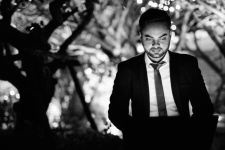 Young bearded Indian businessman against view of the city at night