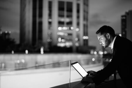 Young bearded Indian businessman against view of the city at nightの写真素材