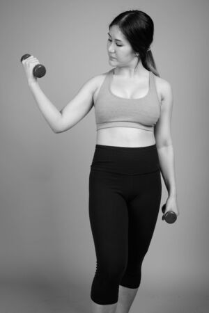 Young beautiful Asian woman ready for gym against gray backgroundの写真素材