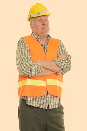Studio shot of mature man construction worker thinking with arms crossed