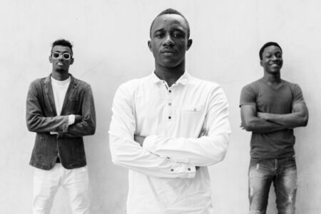Three young African men hanging out against concrete wall outdoorsの写真素材