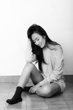 Thoughtful young Asian woman sitting on the floor and looking downの写真素材