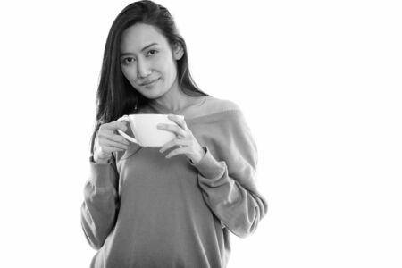 Studio shot of young beautiful Asian woman holding coffee cupの写真素材