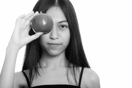 Studio shot of young Asian teenage girl covering eye with red appleの写真素材