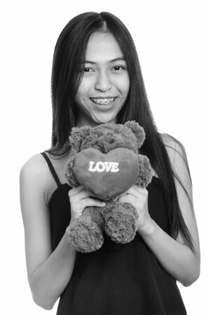 Young happy Asian teenage girl smiling while holding teddy bear with heart and love signの写真素材