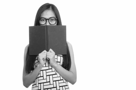 Young Asian teenage nerd girl hiding behind bookの写真素材