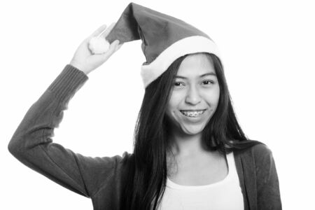 Studio shot of young happy Asian teenage girl smiling while holding hat ready for Christmasの写真素材