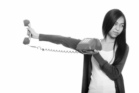 Studio shot of young Asian teenage girl holding old telephone looking annoyed