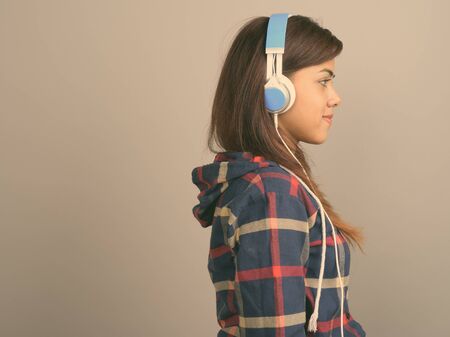 Young beautiful Indian woman listening to music against gray background