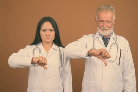 Mature multi-ethnic couple doctors against brown background
