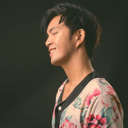 Young handsome Asian man against black background