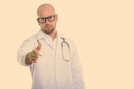 Studio shot of young bald muscular man doctor giving handshakeの写真素材