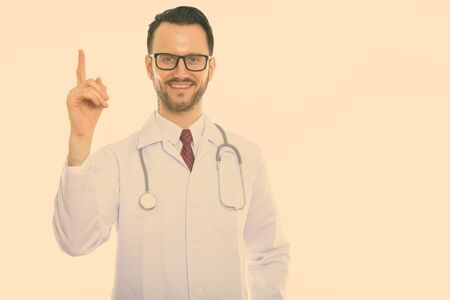 Studio shot of young happy man doctor smiling while pointing finger upの写真素材