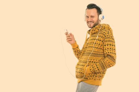 Studio shot of happy young man smiling while holding mobile phone and listening to music