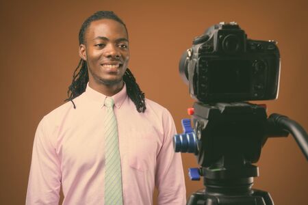 Young handsome African businessman against brown backgroundの写真素材