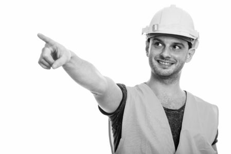 Studio shot of young happy man construction worker smiling while pointing finger
