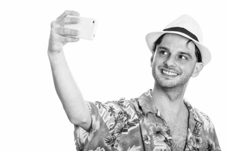Studio shot of young happy man smiling while taking selfie with mobile phoneの写真素材