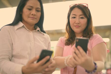 Two mature Asian women together at the skytrain station in Bangkok, Thailandの写真素材