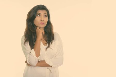 Studio shot of young beautiful Persian woman thinking while looking up isolated against white...