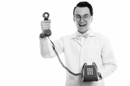 Studio shot of happy crazy man doctor smiling while giving old telephoneの写真素材