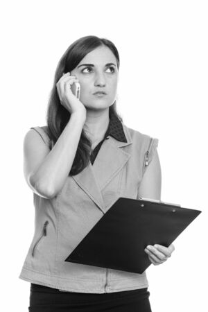 Thoughtful businesswoman talking on mobile phone while holding clipboardの写真素材