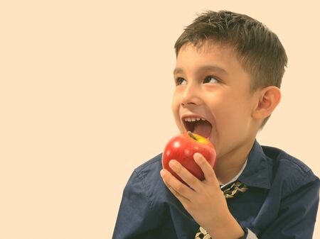Studio shot of cute happy boy smiling and eating apple while thinking