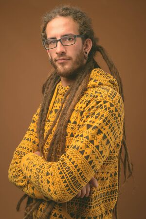 Young handsome Hispanic man with dreadlocks against brown background