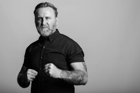 Studio shot of mature bearded man with hand tattoos getting ready to fight in gray backgroundの写真素材