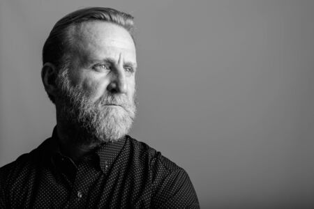 Studio shot of mature bearded man thinking while looking away in gray backgroundの写真素材