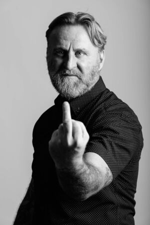 Close up of mature bearded man with hand tattoos showing his middle finger in gray backgroundの写真素材