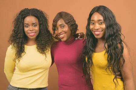 Young beautiful African twin sisters and friend against brown backgroundの写真素材