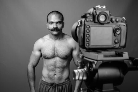 Shirtless muscular Indian man with mustache vlogging against gray backgroundの写真素材