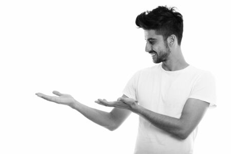 Profile view of young happy Persian man smiling while showing somethingの写真素材